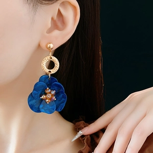 Detail of vintage blue flower earrings with gold accents worn by a model on black background