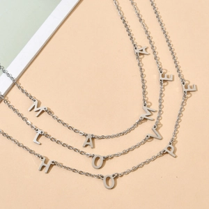 Three minimalist silver stainless steel letter pendant necklaces on warm beige background