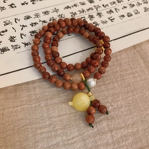 Detail of red-brown wood bead bracelet with a yellow teapot charm on linen fabric