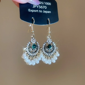 Dettaglio di orecchini vintage argentati con gemme verdi e nappe di perle bianche