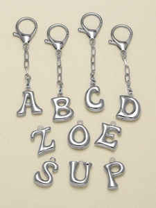 Polished silver alloy alphabet keychains with lobster clasps on beige art paper