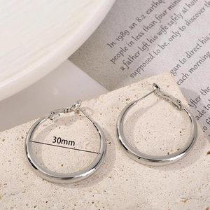 Detail view of 30mm polished silver hoop earrings placed on a natural stone surface