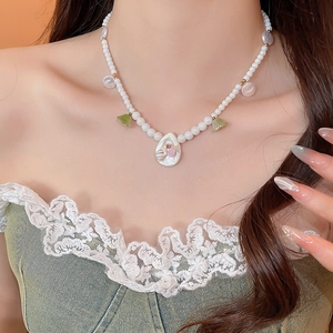 Detail of pearl flower necklace with shell pendant worn on neck against orange backdrop