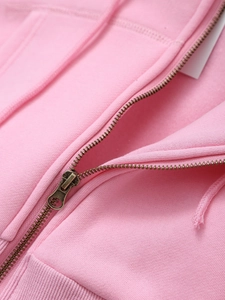Close-up of bronze metal zipper and pink knit fabric detail on casual cropped hoodie