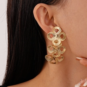 Macro view of gold triple-layered flower earrings with textured petals on model