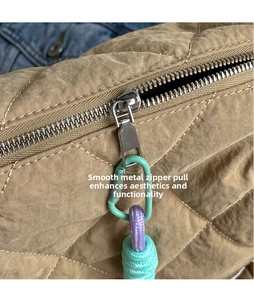 Macro detail of silver zipper and colorful rope charm on quilted khaki tote bag