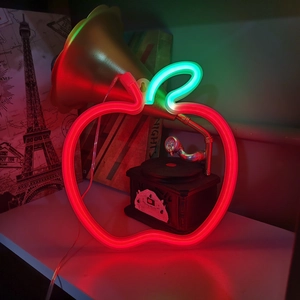Detailed view of red apple neon sign with green leaf on a dark vintage desk setup