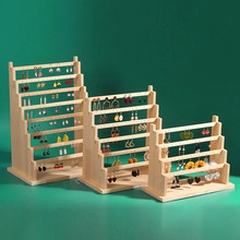 Three-tier wooden earring display stands showing various earring styles on a green background