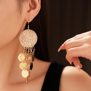 Detail of gold layered round sequins and tassel hook earrings on a female model