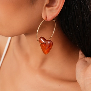 Close-up of a gold hoop earring with a vintage amber resin heart pendant on model