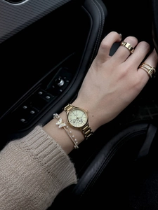 Luxurious gold watch with matching butterfly pearl bracelet and rings on car interior background