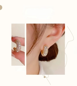 Detail of C-shaped gold hoop earrings featuring micro-paved white cubic zirconia crystals