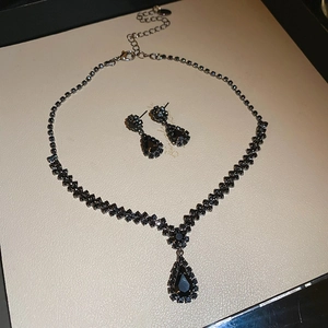 Detailed view of pear-cut black gemstone necklace and earrings set on light textured background
