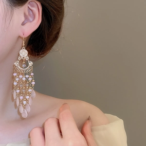 Close-up of bohemian gold earrings with pink beaded tassels and teardrop charms