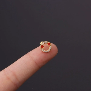 Macro detail of gold helix stud with red star accents and pavé stones held by fingers