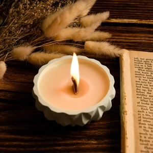 Close-up of a burning wood wick candle in a geometric ceramic jar with scallop edges