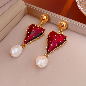 Detailed close-up of red heart earrings with baroque pearls on a velvet jewelry pad