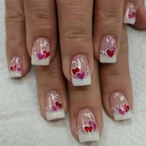 Close-up of French tip press-on nails with red hearts and white swirl patterns