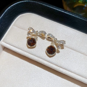 Golden bow earrings with brown round gemstones in a beige velvet jewelry box