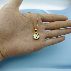 Macro shot of gold cross necklace featuring a white shell pendant held in hand