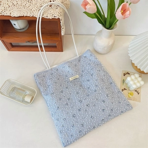 Detail of light blue mesh tote bag with pearl accents and delicate white shoulder strap