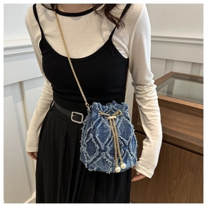 Detail of denim bucket bag with frayed edges, gold chain, and pearl accents on a model