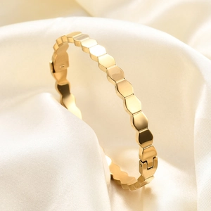 Macro detail of golden hexagonal honeycomb bangle on elegant white silk fabric