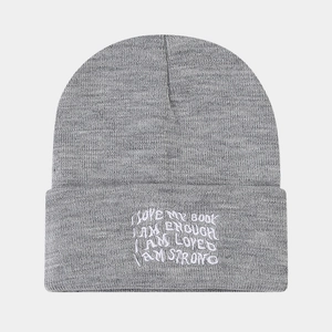 Detail of grey knitted beanie featuring white embroidered motivational text on the cuff