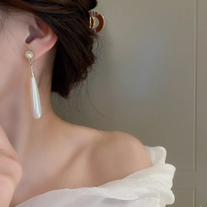 Close-up of elegant long pearl drop earrings with gold connector worn by a model