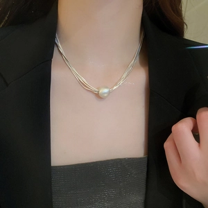 Detail of layered silver snake chains with a large white baroque pearl on a female neck