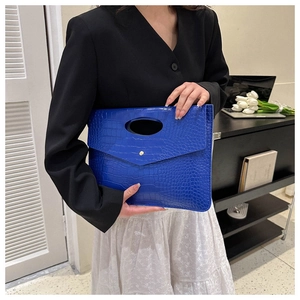 Blue crocodile pattern envelope clutch bag held by model in professional office setting