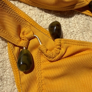 Detail of ribbed yellow bikini featuring dark green resin beads and golden metal rings