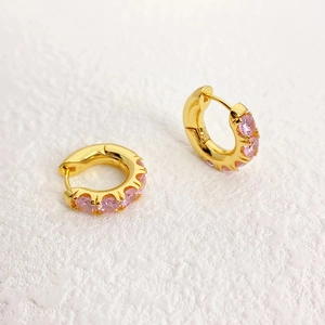 Elegant gold hoop earrings with pink zircon stones on white textured background