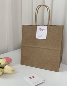 Detail of thank you sticker on brown kraft gift bag with handles and tulips