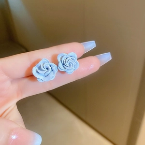 Detailed view of matte blue rose earrings with layered petals in a hand-held close-up shot