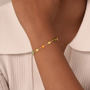 Close-up of golden enamel heart and flower charm bracelet worn on a woman's wrist