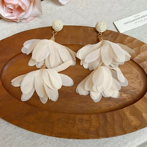 Detail of cream chiffon petal tassel earrings with a 3D rose stud on wooden tray