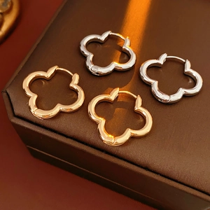 Macro detail of gold and silver hollow clover-shaped hoop earrings on leather