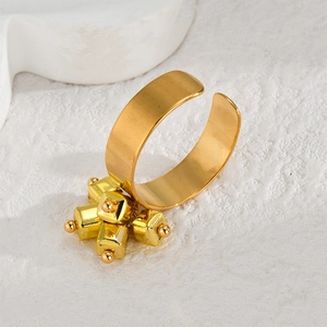 Golden wide band ring with square charm pendants on a white textured background
