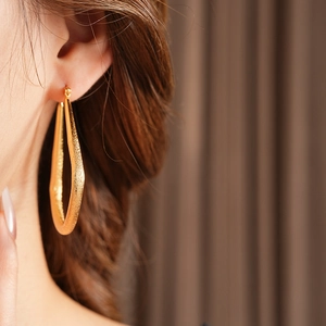 Gros plan d'une boucle d'oreille dorée en forme d'éventail texturé sur mannequin
