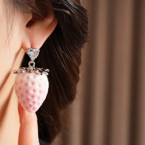 Detail view of a pink strawberry earring with heart-shaped zircon on model's ear