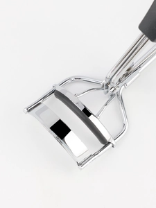 Close-up of stainless steel eyelash curler with black rubber pad and chrome finish