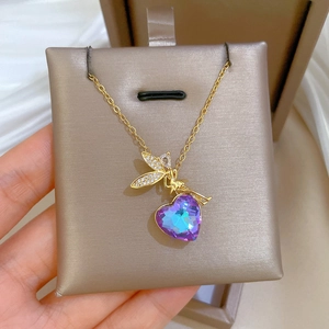 Macro detail of gold angel wing necklace with heart-shaped purple gradient crystal