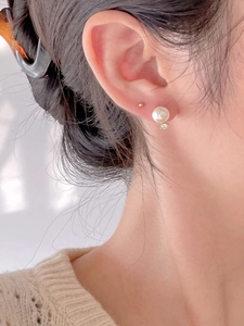Close-up of elegant pearl and gold stud earrings worn on a model's ear for styling