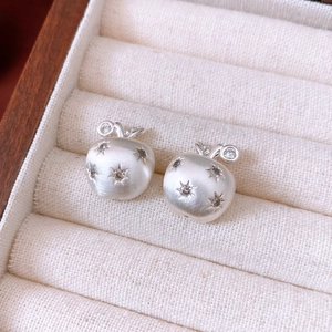 Macro detail of apple-shaped matte silver earrings with brushed metal finish and star zircons