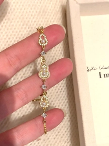 Détail d'un bracelet ajustable en or 18 carats avec pendentifs gourde et perles