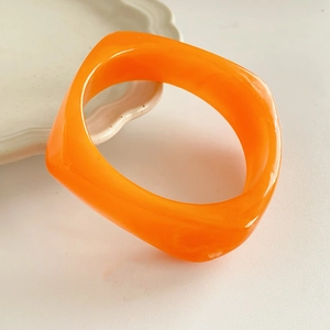 Detail of a bright orange square resin bangle with natural texture on a white plate