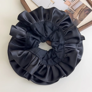 Close-up of black ruffled satin oversized hair scrunchie with glossy silk texture