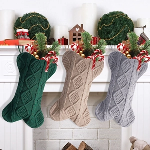Three bone-shaped knitted Christmas stockings in green, beige and grey hung on white fireplace