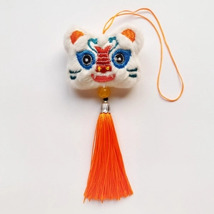 Vue détaillée du charme tête de lion blanc brodé avec glands oranges et perles